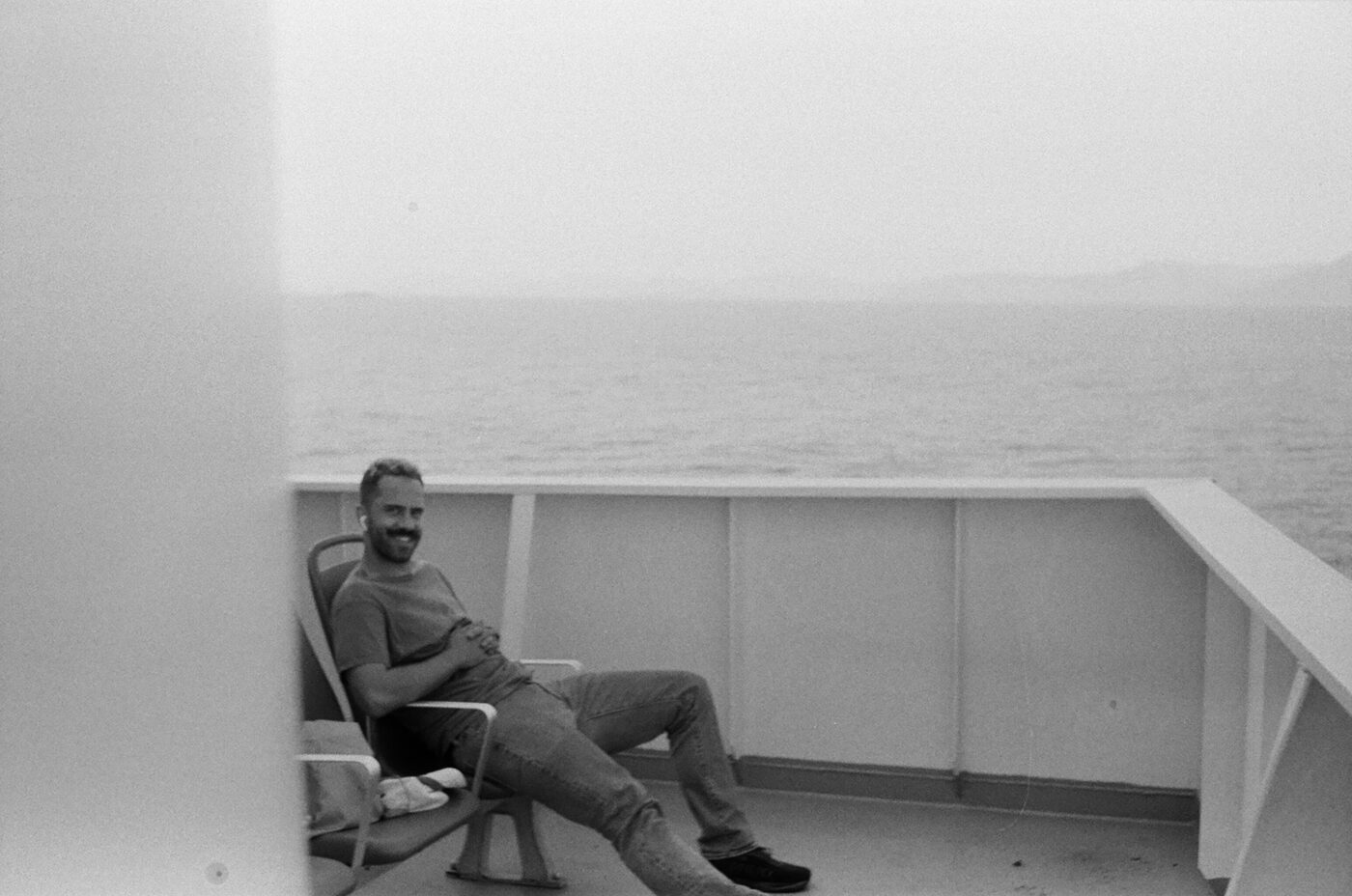 Orfeas smiling while seated on a ferry deck with the sea behind him