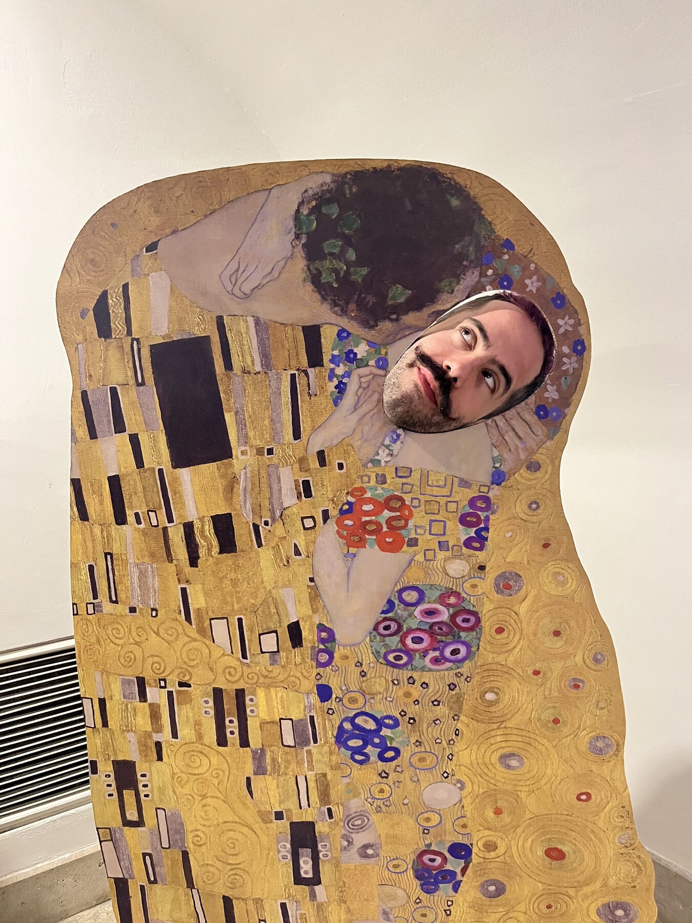 Orfeas posing through a face cutout in a reproduction of The Kiss