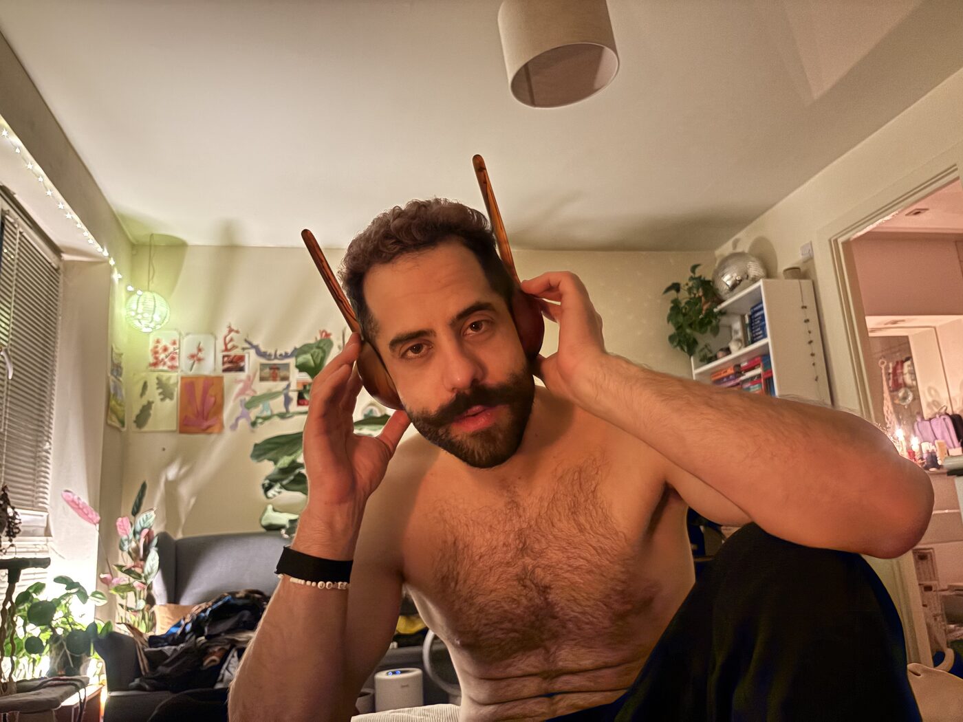 Orfeas holding two wooden sticks against his ears at home